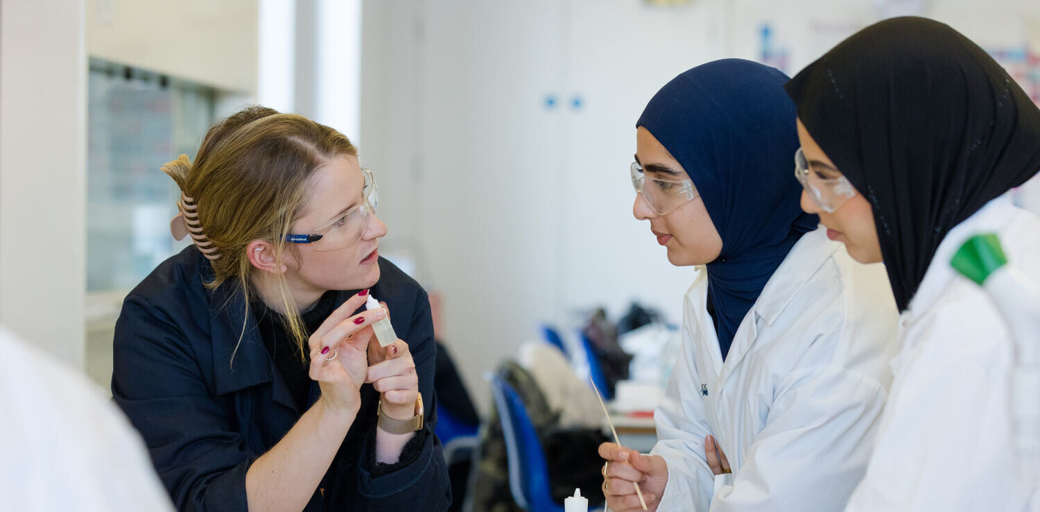 two students in a science lab with their teacher doing a practical